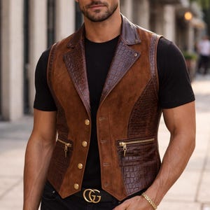 May include: A brown vest featuring a combination of smooth suede and dark brown crocodile-embossed leather panels. The garment includes a notched lapel, four gold-toned buttons, and two zippered pockets with gold hardware, worn over a black t-shirt.