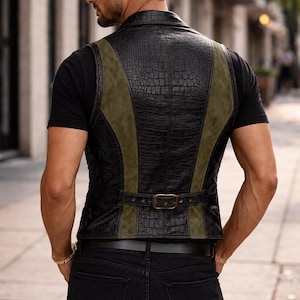 May include: A sleeveless vest featuring a black crocodile-textured pattern on the back and sides, contrasted with olive green suede-like panels. The garment includes a horizontal back strap with a metallic buckle and is worn over a black t-shirt.