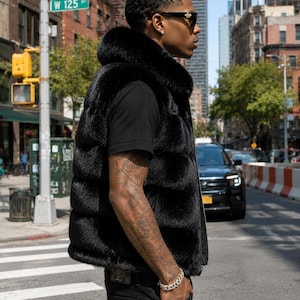 May include: A black fur vest with a high collar. The vest is worn over a black t-shirt and paired with black jeans. The person is wearing sunglasses and a silver bracelet. The background shows a city street with a street sign that reads W 125 ST.