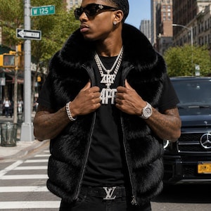 May include: A black fur vest with a zip-up front is worn over a black t-shirt. The vest is paired with black jeans and a belt with a silver buckle. The outfit is accessorized with a silver watch, bracelet, and necklace. The necklace pendant reads "ZRF 4PF".