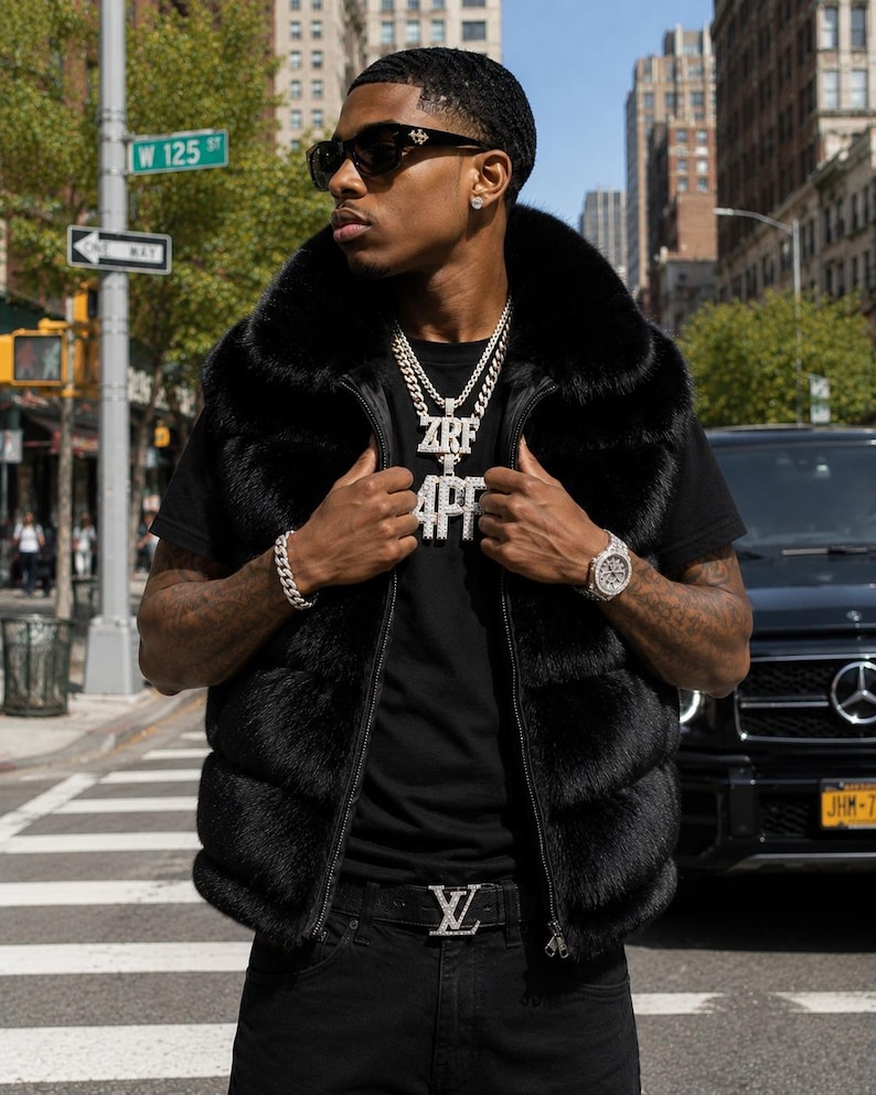 May include: A black fur vest with a zip-up front is worn over a black t-shirt. The vest is paired with black jeans and a belt with a silver buckle. The outfit is accessorized with a silver watch, bracelet, and necklace. The necklace pendant reads "ZRF 4PF".