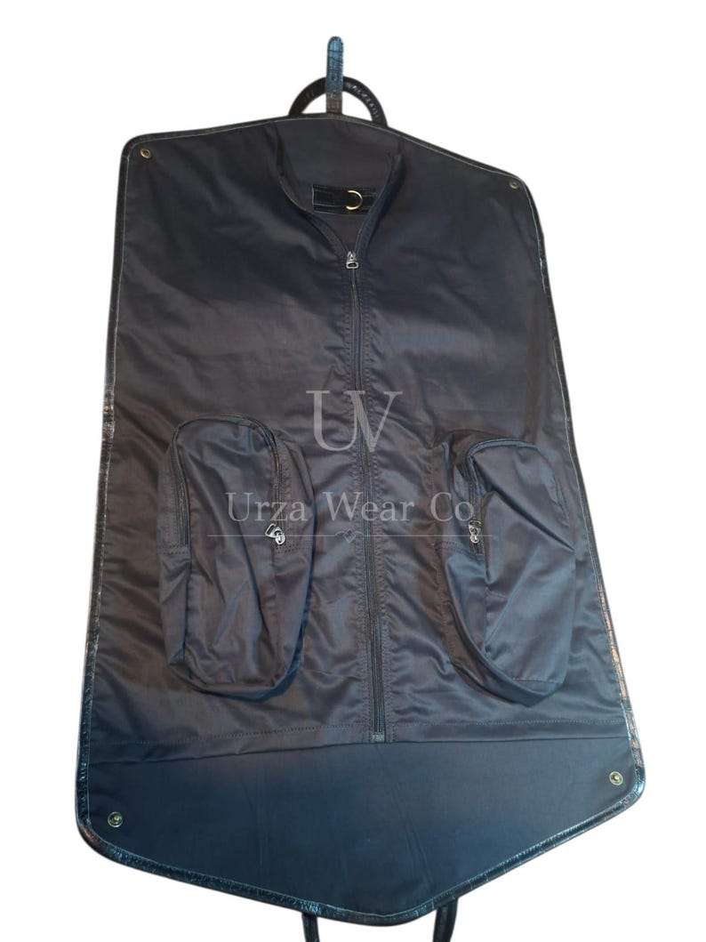 May include: A black garment bag featuring a central vertical zipper, two exterior zippered pockets, and a top hanging loop. The text "UV" and "Urza Wear Co" are printed in white on the front surface of the bag.