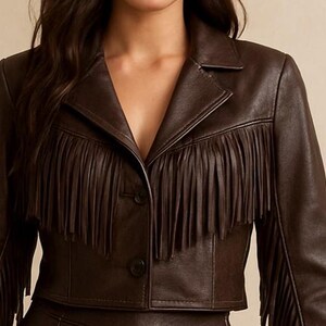 May include: A brown leather jacket with fringe detailing across the chest and sleeves. The jacket has a notched collar and two buttons. The cropped jacket is a stylish outerwear piece.
