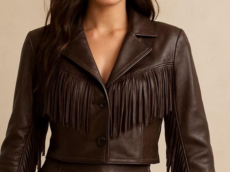 May include: A brown leather jacket with fringe detailing across the chest and sleeves. The jacket has a notched collar and two buttons. The cropped jacket is a stylish outerwear piece.
