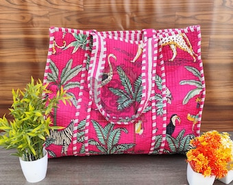 May include: A large, quilted tote bag with a vibrant pink background and a tropical print featuring palm trees, zebras, leopards, and toucans. The bag has white and pink striped handles and trim. The bag is sitting on a wooden surface.