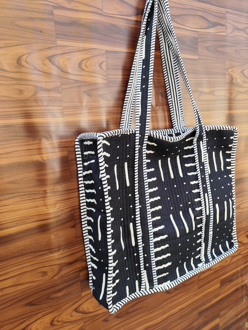May include: A black and white tote bag with a geometric pattern. The bag features a repeating design of vertical and horizontal white lines on a black background. The handles and edges are also white and black striped.