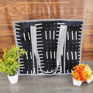 Può includere: Borsa tote nera con motivi verticali e puntinati bianchi. La borsa ha manici e finiture a righe bianche. La borsa è su una superficie di legno con piccole piante in vaso su entrambi i lati.