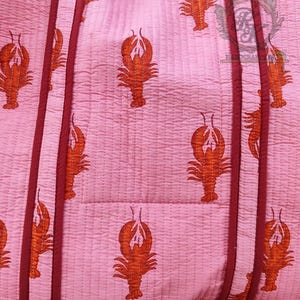 May include: Pink quilted tote bag with a repeating pattern of orange lobsters. The bag has burgundy trim and handles. The bottom of the bag has a burgundy ruffle.