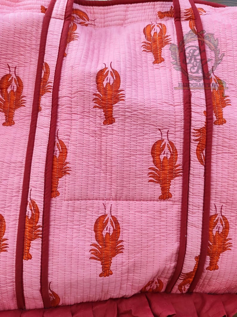 May include: Pink quilted tote bag with a repeating pattern of orange lobsters. The bag has burgundy trim and handles. The bottom of the bag has a burgundy ruffle.