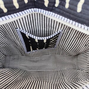 May include: Interior view of a black and white patterned tote bag. The bag features a white zipper and a small pocket with a black and white design. The lining has black and white vertical stripes.