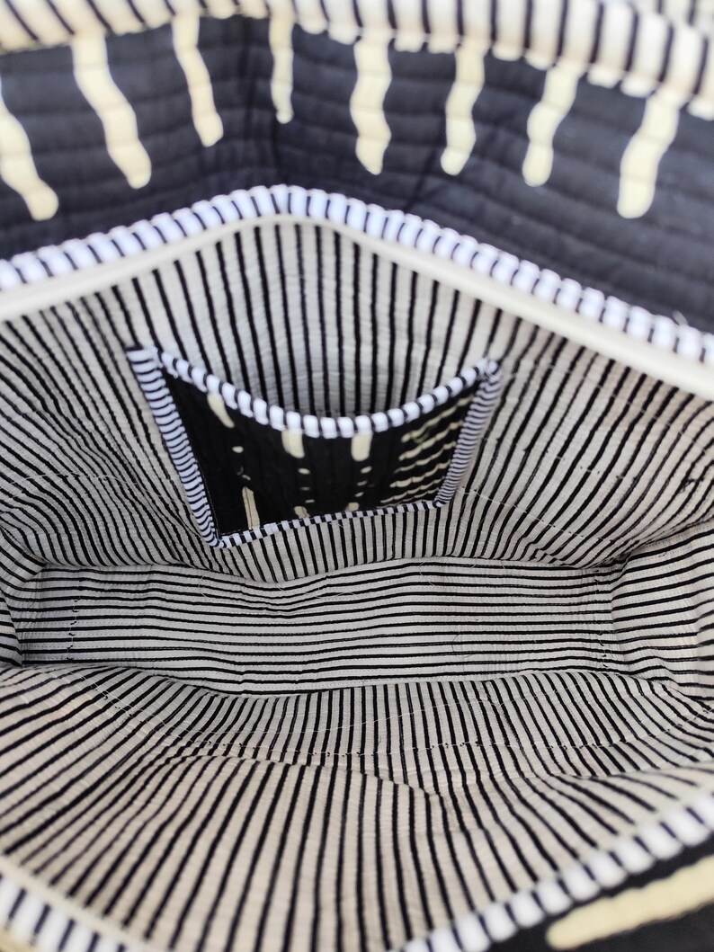 May include: Interior view of a black and white patterned tote bag. The bag features a white zipper and a small pocket with a black and white design. The lining has black and white vertical stripes.