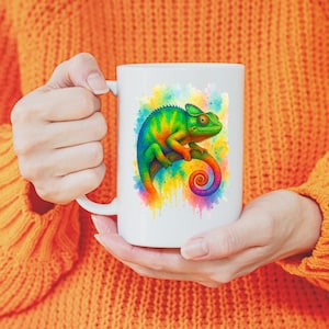 Könnte beinhalten: Weiße Keramik-Tasse mit einer farbenfrohen Chamäleon-Illustration. Das Chamäleon ist in Grün-, Blau- und Gelbtönen dargestellt und sitzt auf einem Ast vor einem Aquarell-Spritzer-Hintergrund. Die Tasse hat einen Standardgriff und eine glänzende Oberfläche.
