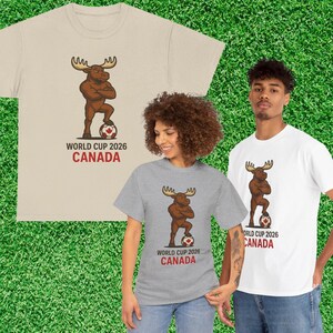 May include: Three t-shirts in beige, gray, and white, each featuring a cartoon moose with crossed arms, standing on a soccer ball. The text "WORLD CUP 2026 CANADA" is printed below the moose in black and red.