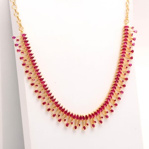 May include: A gold-colored necklace and matching earrings set. The necklace and earrings are adorned with numerous small, vibrant red gemstones. The jewelry is displayed against a white background, highlighting the intricate design and color.