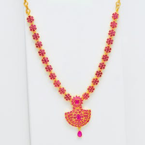May include: A gold-toned necklace featuring a series of small, pink flower-shaped gemstones. The necklace has a pendant with a larger, fan-shaped design, also adorned with pink gemstones, and a teardrop-shaped gemstone at the bottom.