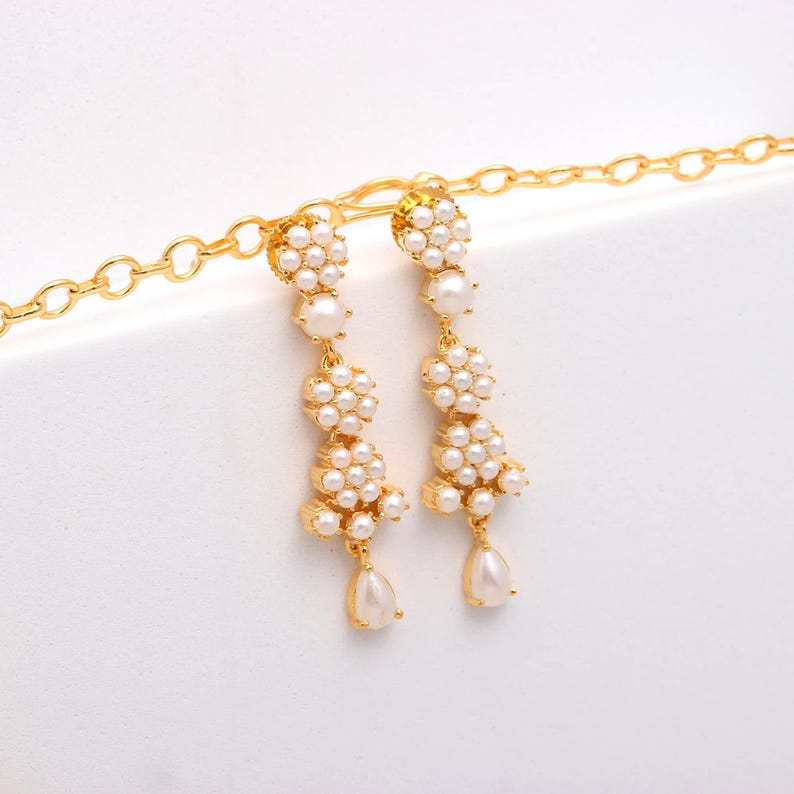 May include: Gold-toned drop earrings featuring clusters of small, round pearls and larger, teardrop-shaped pearls. The earrings have a floral design and hang from a delicate gold chain, creating an elegant and sophisticated look.