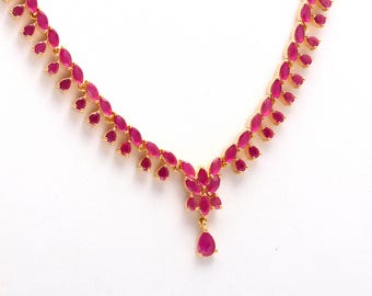 May include: A gold-toned necklace featuring a series of marquise-cut, ruby-colored gemstones. The necklace has a central pendant with a cluster of gemstones and a teardrop-shaped ruby. The design is symmetrical and elegant.