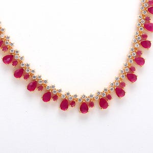 May include: A gold necklace with ruby-red, teardrop-shaped gemstones and clear crystal accents. The necklace's design features a repeating pattern of ruby drops and crystal clusters, creating a sophisticated and attractive piece of jewellery.