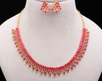 May include: A gold-toned necklace and matching earrings set. The necklace and earrings feature a series of pink, teardrop-shaped gemstones. The jewelry is displayed on a white mannequin bust against a black background.
