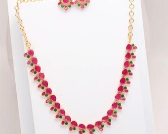 May include: A gold-toned necklace and matching earrings set. The necklace and earrings feature a pattern of pink teardrop-shaped stones with green accents. The jewelry is displayed on a white surface.