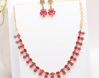May include: A gold-toned necklace and earring set. The necklace and earrings feature a repeating pattern of red and green gemstones. The earrings are dangling, and the necklace is a choker style.