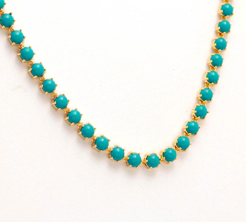 Op de afbeelding: Een goudkleurige ketting met levendige turquoise kralen. Elke kraal is gezet in een delicate, goudkleurige zetting, waardoor een continue, elegante ketting ontstaat. De ketting wordt gepresenteerd tegen een witte achtergrond.