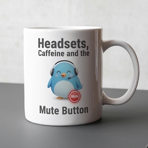May include: White ceramic mug featuring a cartoon penguin wearing a headset. The mug has the text "Headsets, Caffeine and the Mute Button". The penguin has a blue body, white belly, and is holding a red "Mute" button.