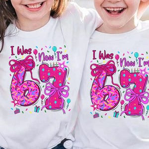 May include: White t-shirts with a colorful birthday design. The shirts feature the text "I Was Now I'm" above a large pink "67" with sprinkles, bows, and birthday decorations. Perfect for a birthday celebration.