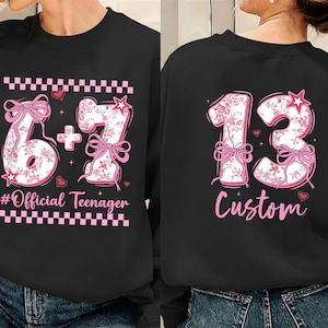 May include: Black sweatshirt with a pink floral design. The front features the numbers 6 + 7 with bows and the text "#Official Teenager". The back displays the number 13 with the word "Custom".