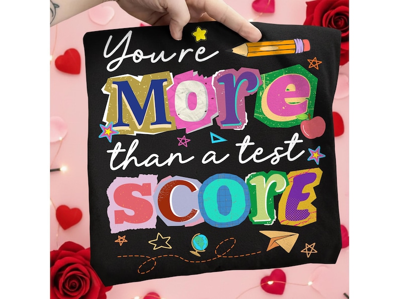 May include: Black t-shirt with the text "You're More than a test SCORE" in colorful, layered letters. A pencil graphic and various stars, a globe, and a paper airplane are also featured.