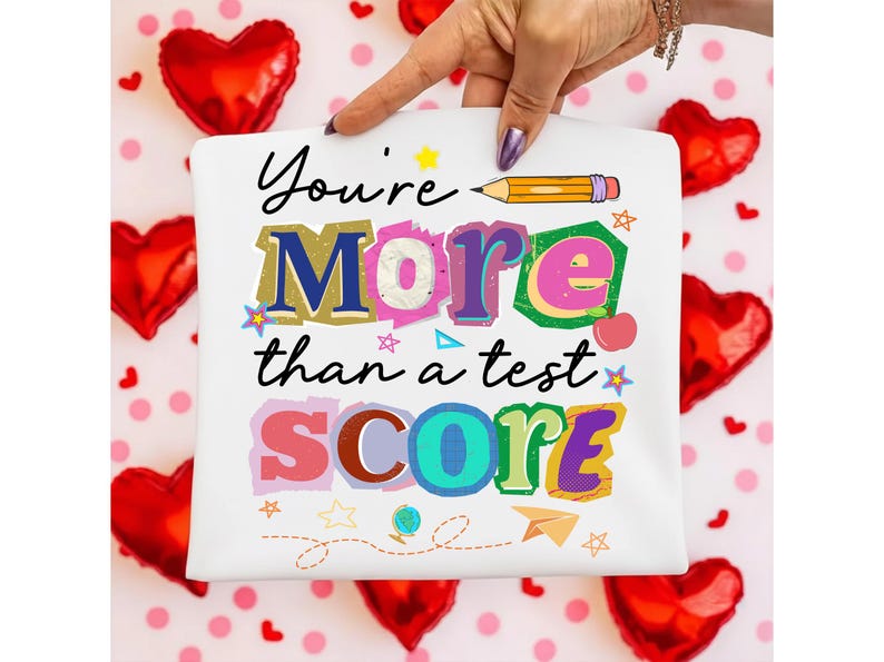 May include: White square with the text "You're More than a test SCORE" in colorful, playful lettering. A yellow pencil graphic is above the word "More". The background includes red heart-shaped balloons and pink polka dots.
