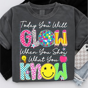 May include: Dark gray sweatshirt with the text "Today You Will GLOW When You Show What You KNOW." The word "GLOW" has a disco ball, and the word "KNOW" has a smiley face. The sweatshirt is a casual style.