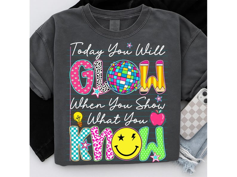 May include: Dark gray sweatshirt with the text "Today You Will GLOW When You Show What You KNOW." The word "GLOW" has a disco ball, and the word "KNOW" has a smiley face. The sweatshirt is a casual style.
