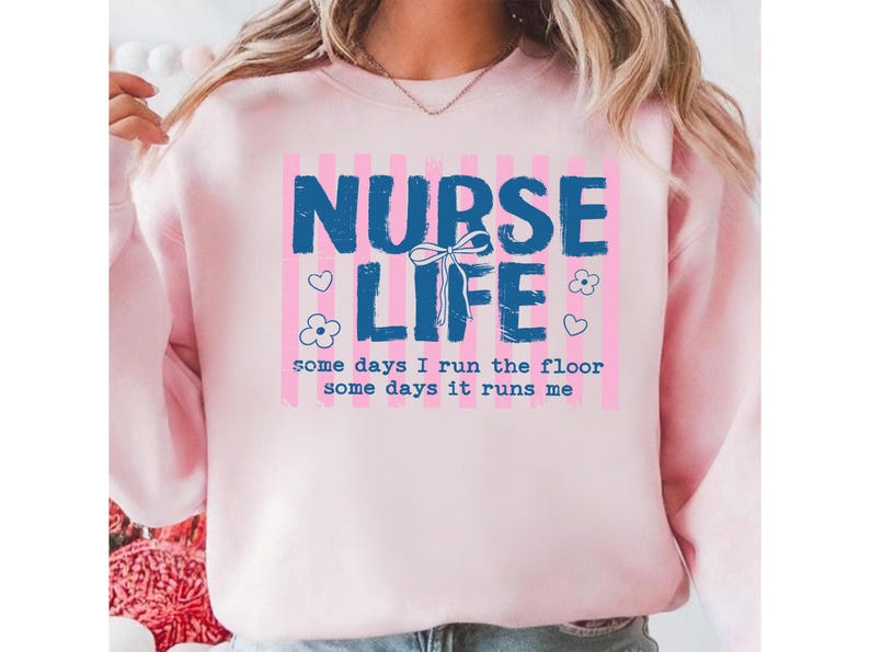 May include: A light pink sweatshirt with the words "NURSE LIFE" in blue block letters. The text is set against a pink and white striped background. The phrase "some days I run the floor some days it runs me" is below.