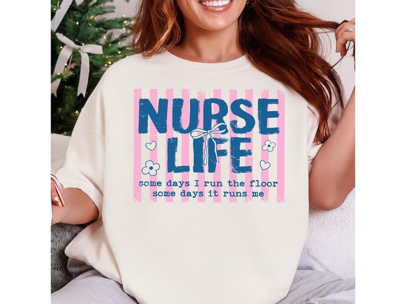 May include: Cream-colored sweatshirt with the words "NURSE LIFE" in blue block letters, set against pink striped background. The text "some days I run the floor some days it runs me" is below. Floral and heart graphics are also present.