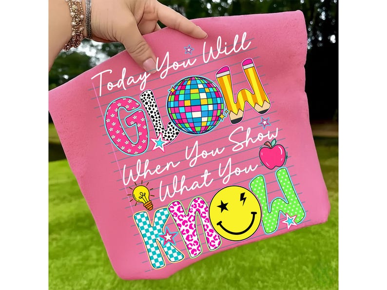 May include: Pink pillow with the text "Today You Will GLOW When You Show What You KNOW." The word "GLOW" has a disco ball design. The word "KNOW" has a smiley face design. Other graphics include pencils, stars, an apple, and a lightbulb.