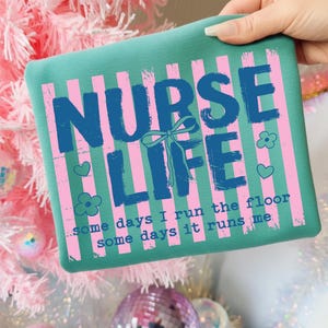 May include: Teal square pillow with pink vertical stripes and the words "NURSE LIFE" in blue. The text "some days I run the floor, some days it runs me" is also printed on the pillow. Decorative hearts and flowers are also included.