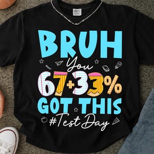 May include: Black t-shirt with the text "BRUH You 67+33% GOT THIS #Test Day" in blue, white, and yellow. The design includes stars, a paper airplane, a lightbulb, and an apple.