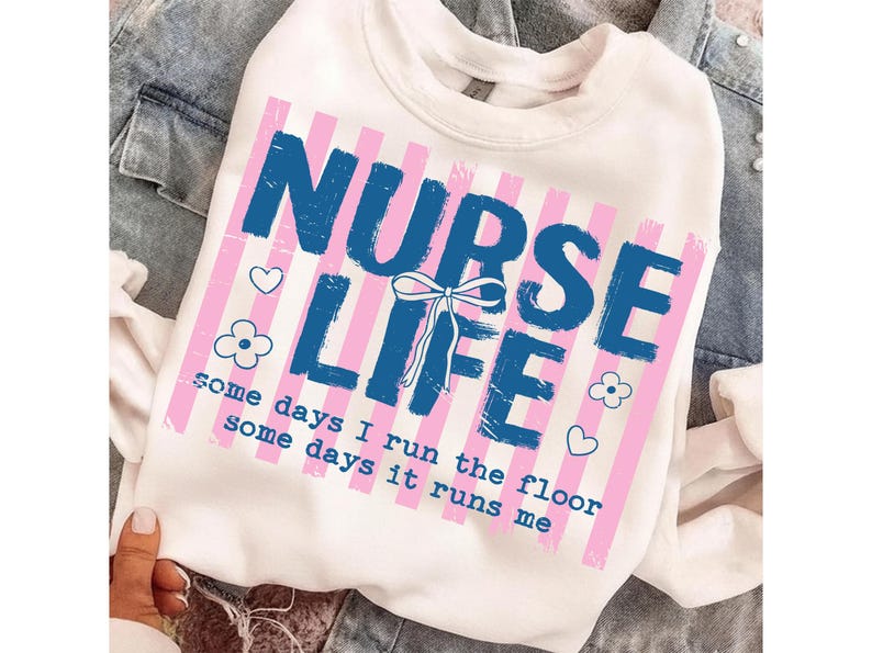 May include: White sweatshirt with a graphic that reads "NURSE LIFE" in blue, with pink vertical stripes. The text "some days I run the floor some days it runs me" is below the main text. Small heart and flower graphics are also included.