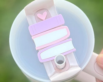 May include: A light pink tumbler lid with a heart-shaped accent and a sliding closure. The lid features pastel-coloured, rectangular sliders in lavender, white, and pink. The tumbler is partially filled with a clear liquid.
