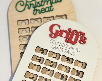 May include: White wooden countdown calendar with bone-shaped openings. The calendar says "Griff's Countdown to Santa Paws".