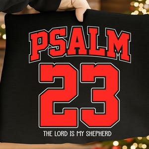 Könnte beinhalten: Schwarzes Kissen mit dem Text "PSALM 23" in Rot und Weiß, mit der Zahl "23" in großer, fetter Schrift. Der Satz "THE LORD IS MY SHEPHERD" ist darunter gedruckt.