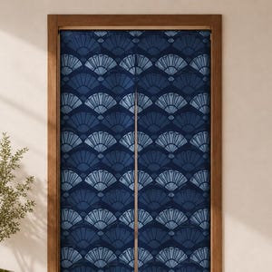 Op de afbeelding: Een blauw en wit patroon deur gordijn met een ventilator ontwerp. Het gordijn hangt in een houten deurkozijn. Een kleine potplant staat links van de deur.