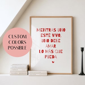 May include: A framed wall art print featuring the red text "MIENTRAS UNO ESTÉ VIVO, UNO DEBE AMAR LO MÁS QUE PUEDA" with a small red heart at the bottom. A pink circular graphic on the left displays the text "CUSTOM COLORS POSSIBLE".