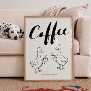 Könnte beinhalten: Ein gerahmter Druck mit dem Wort "Coffee" in großer schwarzer Schrift. Zwei Cartoon-Enten halten Kaffeetassen, mit dem Text "Everything else can wait." Ein Dalmatiner-Hund liegt im Hintergrund auf einem beigen Sofa.