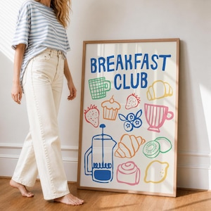 Könnte beinhalten: Ein gerahmtes Poster mit den Worten "BREAKFAST CLUB" in Blau, das farbenfrohe Illustrationen von Frühstücksartikeln wie einer Kaffeepresse, einem Croissant und Obst zeigt. Das Poster befindet sich in einem hellen Holzrahmen.