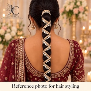 May include: A long dark hair braid wrapped in a decorative gold-toned spiral accessory featuring small white pearls and circular mirrors. The hair is styled with gold-toned dangling earrings and a deep maroon garment with intricate gold embroidery.