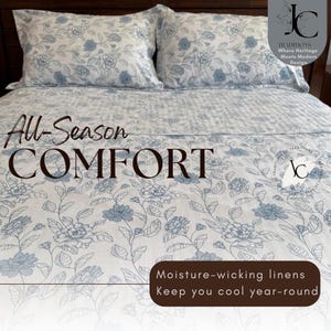 May include: A white bedspread and two matching pillowcases featuring a blue floral pattern. The text reads All-Season COMFORT, Moisture-wicking linens Keep you cool year-round, and Traditions Where Heritage Meets Modern Design with a JC logo.