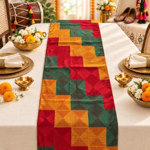 May include: A rectangular table runner featuring a geometric pattern of alternating squares in deep red, emerald green, and golden yellow. The fabric has a subtle sheen and a textured weave, laid flat across a white tablecloth with a festive arrangement.