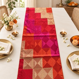 May include: A rectangular table runner featuring a geometric patchwork design in vibrant shades of red, pink, and orange, accented with metallic gold thread embroidery in a repeating diamond pattern across the fabric surface.